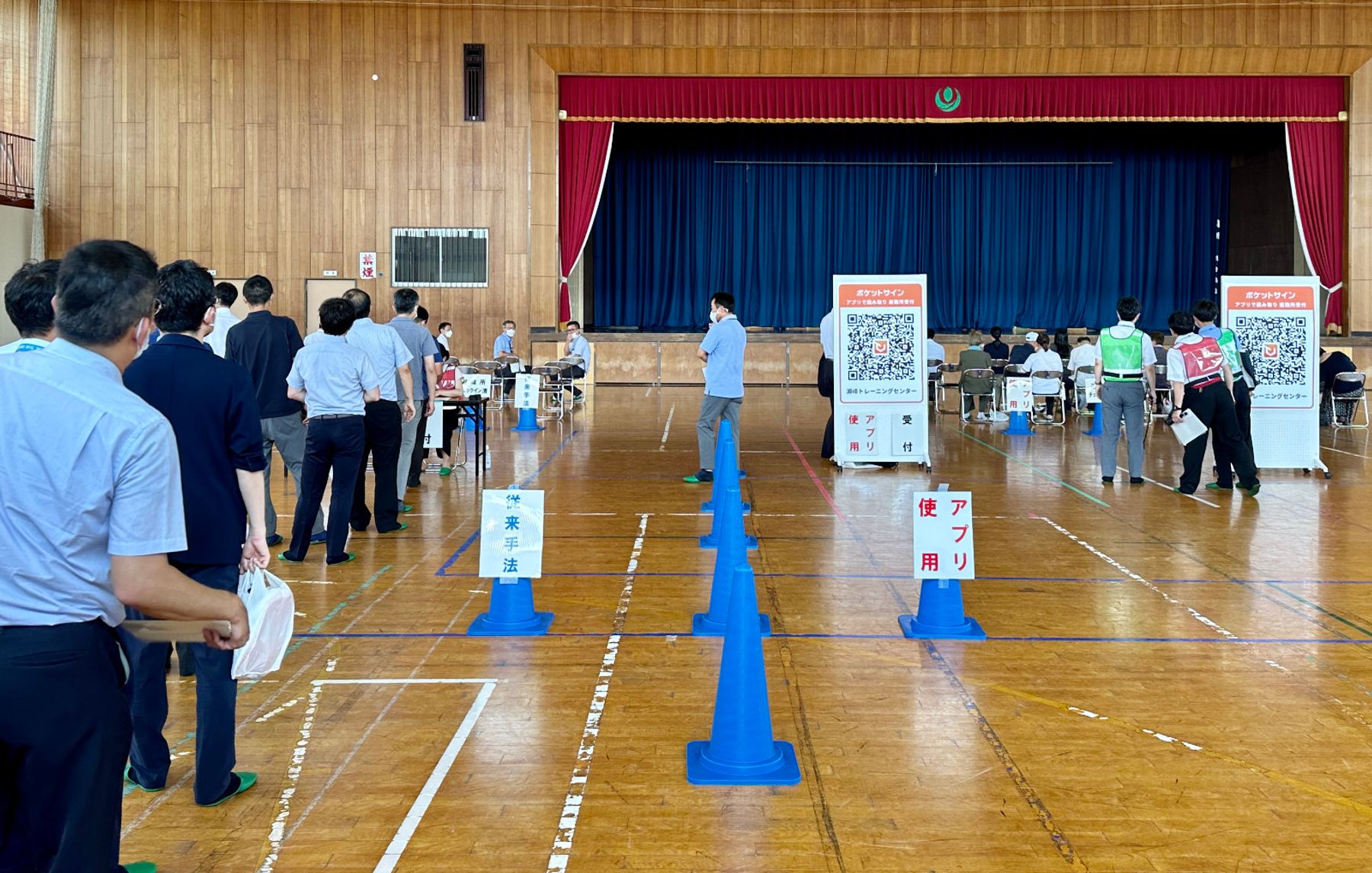 避難所での受付比較：アプリでのチェックインが完了する一方、従来手法ではチェックイン未完了者の列ができている（左：従来手法　右：アプリ使用）